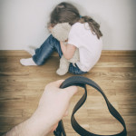 Little girl crying in corner; hand with strap in front