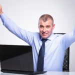 Man sitting at the desk and cheering from behind his laptop