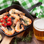 Grilled shrimps on frying pan and beer on wooden table for meal during training session