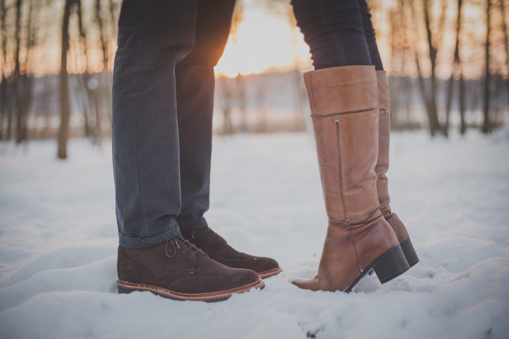 snow; man's boots facing woman's boots. Her standing on tiptoes intimates they are kissing.