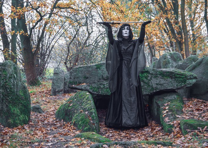 black-robed occult figure with hands upraised in woods and boulders by Marco Federmann