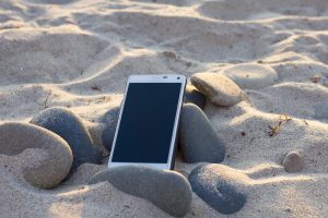 cell phone lying in sand and beach rocks - Pixabay