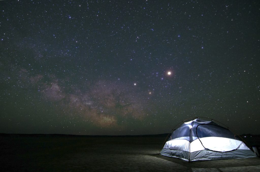 A clear plastic tent on earth, backlit by the night sky full or stars - photo by Pexels