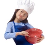 Young Girl in chef's hat stirring mixture in a red bowl for Baking